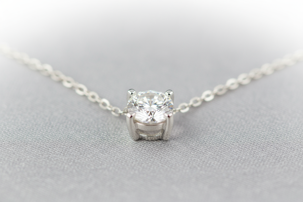 Create an elegant image of a small solitaire round diamond necklace with a 4 prong setting in white gold with a white gold cable chain