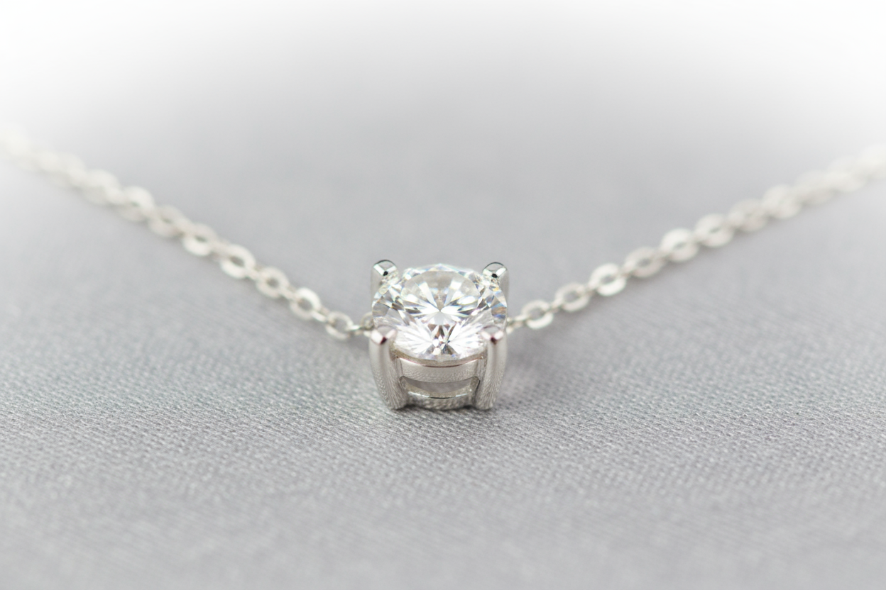 Create an elegant image of a small solitaire round diamond necklace with a 4 prong setting in white gold with a white gold cable chain